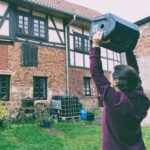 Mitgenosse standing in front of window, playing music from a PA.
