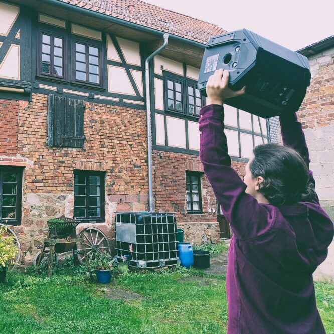 Mitgenosse standing in front of window, playing music from a PA.